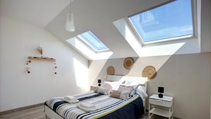 Un dormitorio con tragaluces, una cama con ropa de cama a rayas, una mesita de noche y una mesilla.