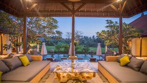 A covered outdoor seating area with a pool, wicker furniture, and a view of the surrounding greenery. - Bali style villa 5 minutes from ubud center! (Ubud)