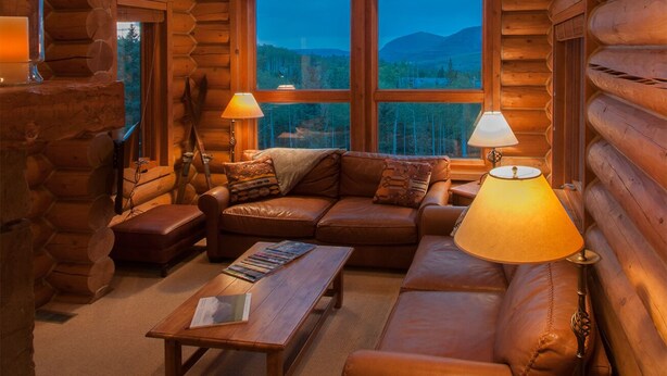 A log cabin interior with a large window, a sofa, a coffee table, and two lamps.