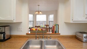 A kitchen with a double sink, a coffee maker, and a toaster. There are windows with blinds, a chandelier, and a bookshelf with books. - Walking trails nearby, Spacious, light filled, well stocked  (Santa Fe)