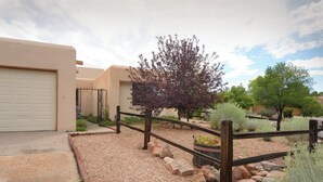 A residential area with a gravel driveway, a wooden fence, and a variety of plants and trees. - Walking trails nearby, Spacious, light filled, well stocked  (Santa Fe)
