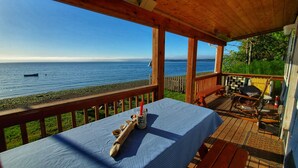 A wooden deck with a table set for dining, overlooking a calm sea with a boat in the distance. - Waterfront Puget Sound cabin, minutes from Bainbridge Ferry to downtown Seattle (Suquamish)