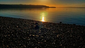 A beach with pebbles and a calm sea reflecting the sun. - Waterfront Puget Sound cabin, minutes from Bainbridge Ferry to downtown Seattle (Suquamish)