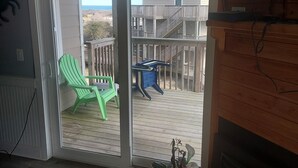 Una habitación con puerta corrediza de vidrio que da a una terraza de madera con mobiliario exterior.