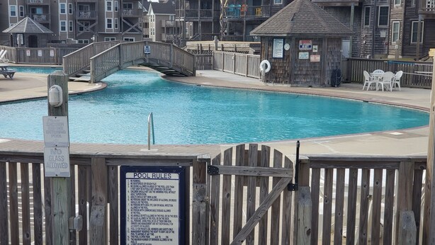 Un área de piscina de madera con un puente, edificios de madera y un letrero que enumera las normas de la piscina.