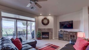 A living room with a fireplace, a television, and a large window overlooking a landscape.