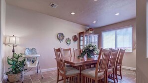 A dining area with a wooden table and chairs, a potted plant, a cabinet, and a window with blinds.