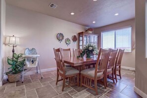 A dining area with a wooden table and chairs, a potted plant, a cabinet, and a window with blinds.
