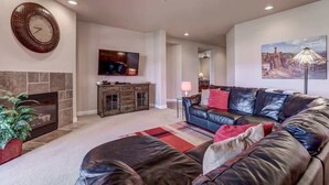 A living room with a fireplace, a leather sofa, a television, and a ceiling fan.