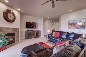 A living room with a fireplace, a leather sofa, a television, and a ceiling fan.