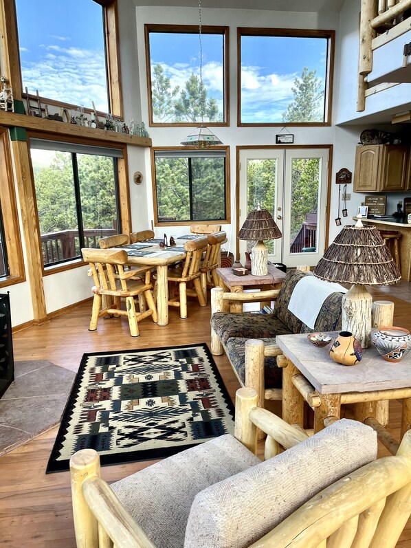 A spacious room with large windows, a wooden dining table, chairs, and a sofa.