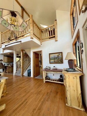 A spacious living area with a wooden staircase, a dining area, and a kitchen visible in the background.