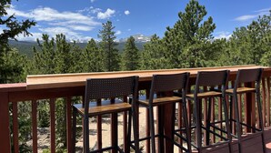 A wooden deck with a table and four chairs, overlooking a mountainous landscape with trees and a clear sky. - Stunning Views Of The Indian Peaks On Mountain Lake (Ward)
