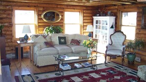 L’intérieur d’un chalet confortable, avec des murs en bois, un canapé, des fauteuils, une table basse et une bibliothèque.