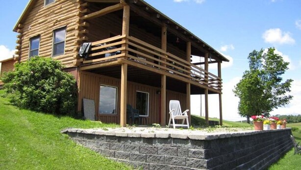 Une cabane en bois avec une véranda, un mur de soutènement en pierre et une pelouse verdoyante.