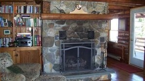 L’intérieur chaleureux d’un chalet avec une cheminée en pierre, un paravent de cheminée, une bibliothèque remplie de livres et un coin salon confortable.
