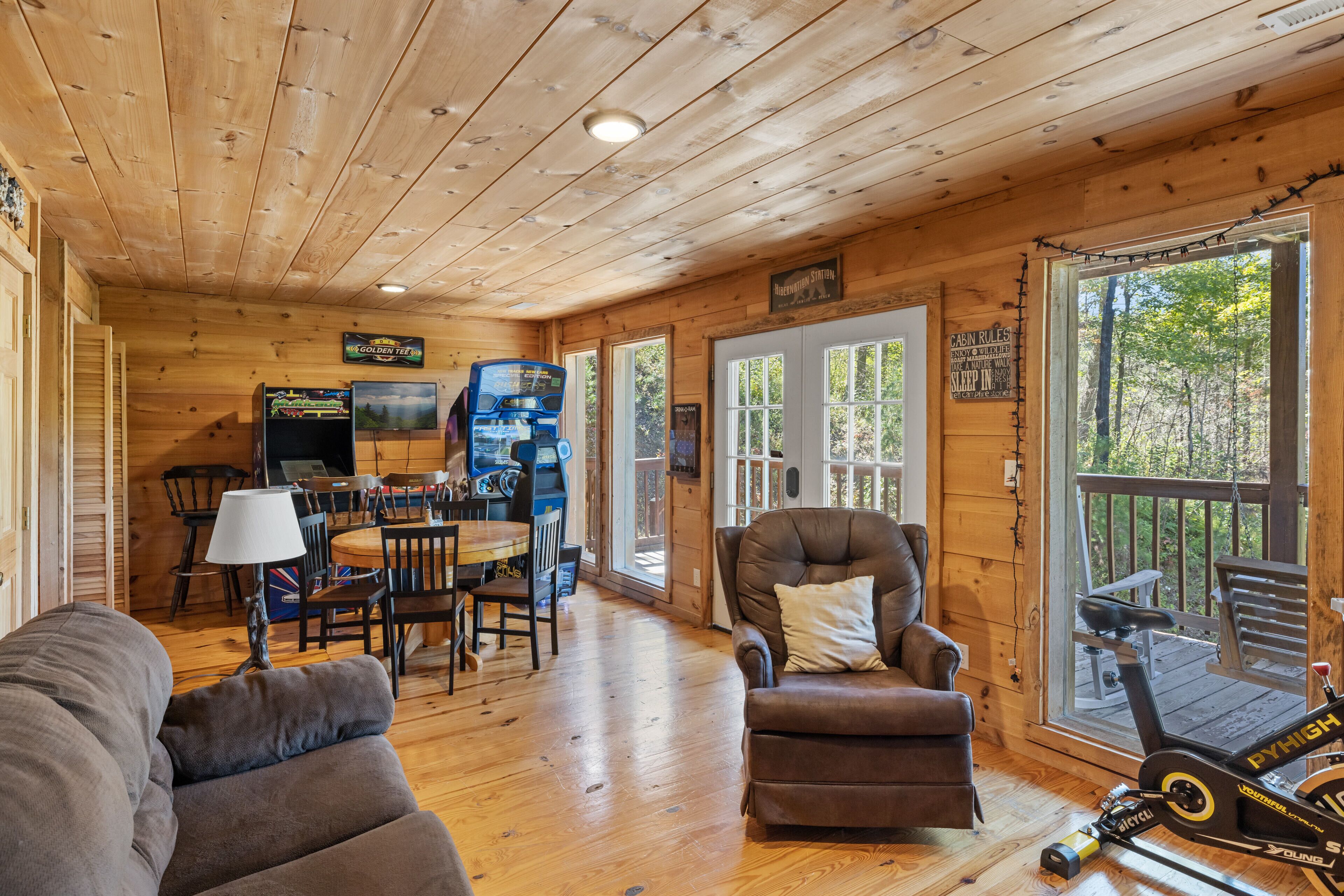 A wooden cabin interior with a dining area, a couch, a recliner, and a treadmill.