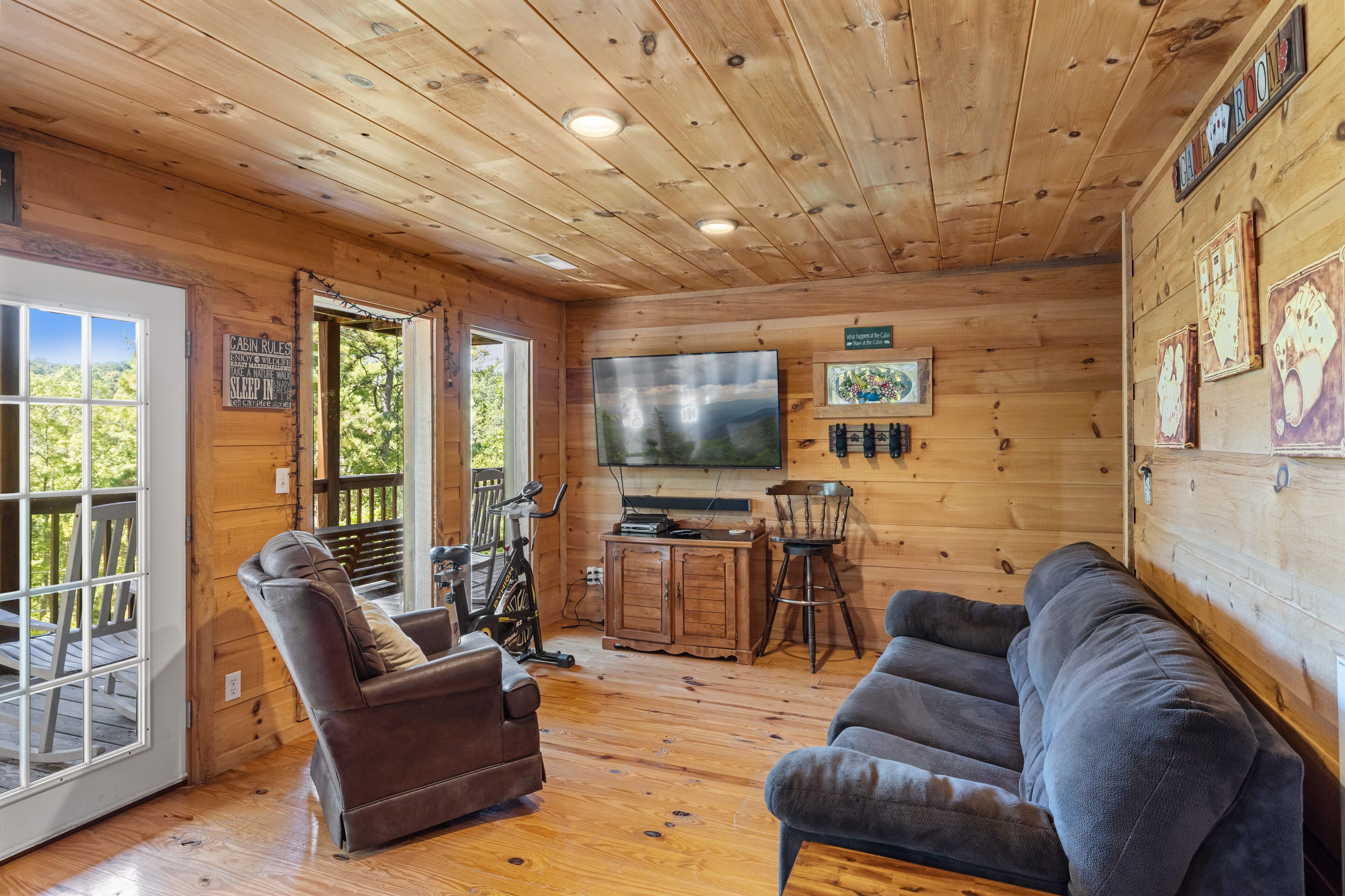Ein Interieur einer Hütte mit Holzbalkendecke, einem Fernseher, einer Couch, einem Sessel und einem Fahrrad.