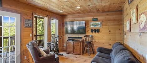 A cabin interior with a wooden ceiling, a television, a couch, a chair, and a bicycle.