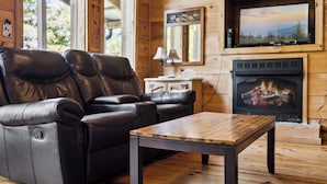 Un interior de madera con un sillón de cuero reclinable, una mesa de centro de madera, una chimenea y un televisor montado encima.