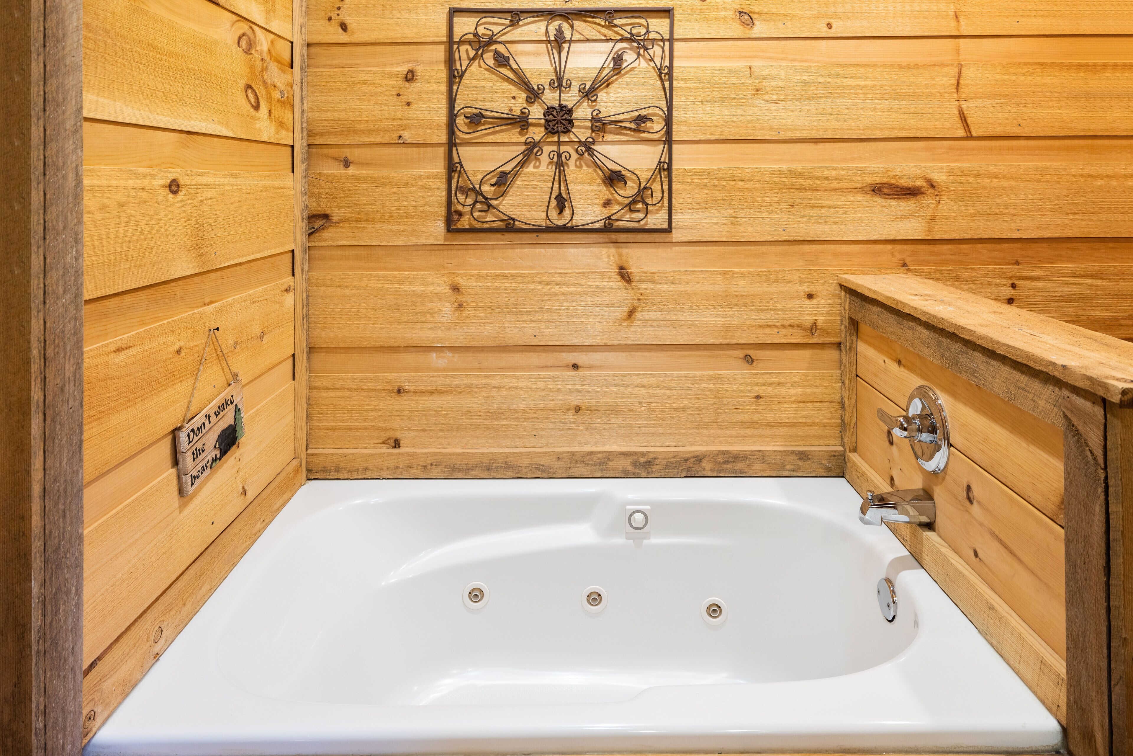 A wooden cabin bathroom with a white bathtub, wooden walls, and a decorative metal piece above the tub.