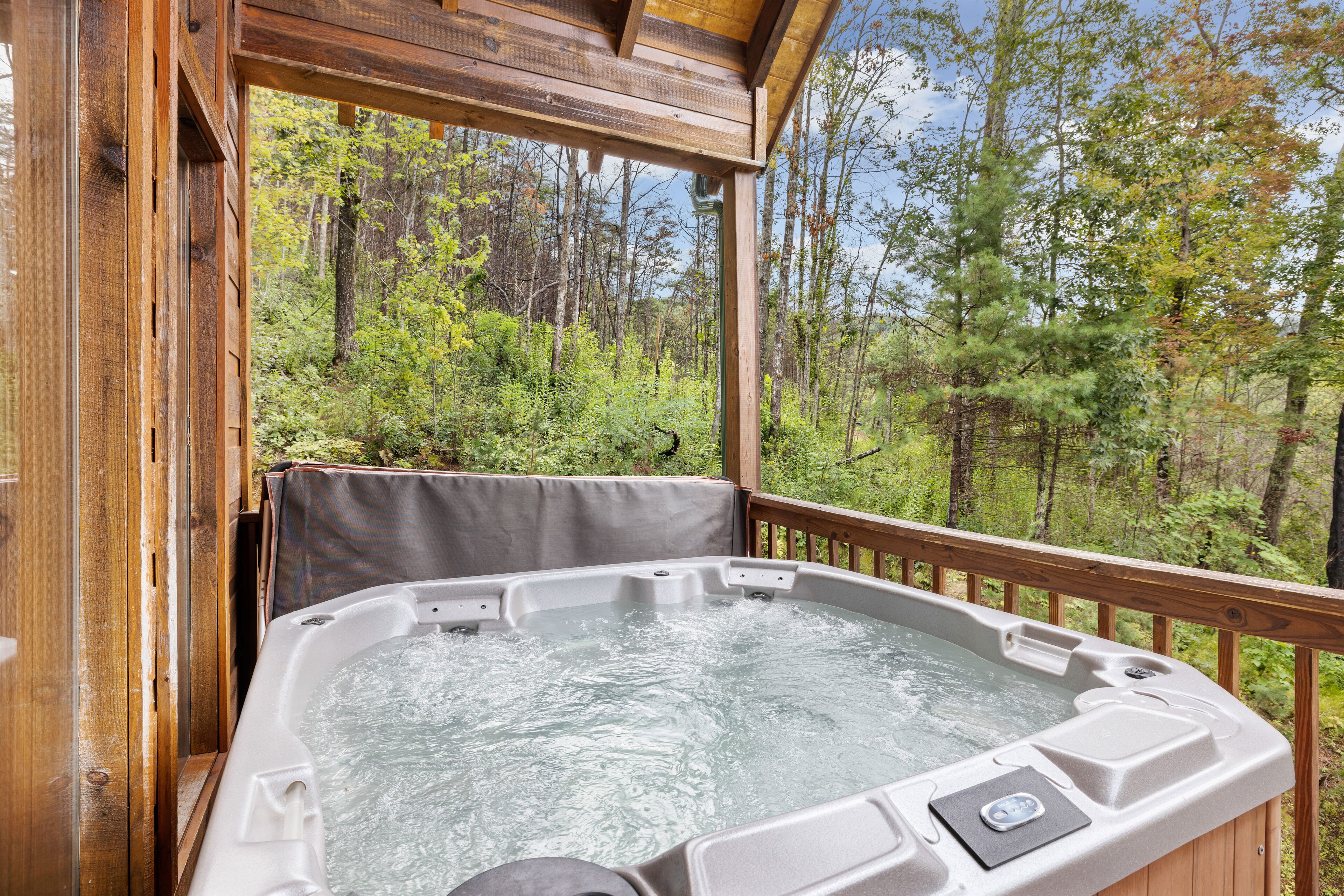 A hot tub with a wooden deck and a view of a forest.