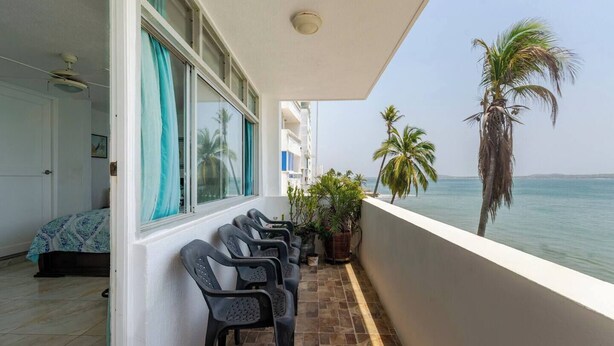 Un balcon avec des chaises, un lit et une vue sur la mer et les palmiers.
