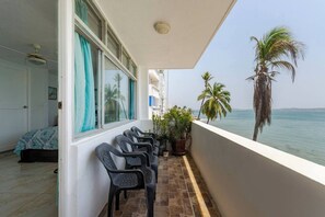 Un balcon avec des chaises, un lit et une vue sur la mer et les palmiers.