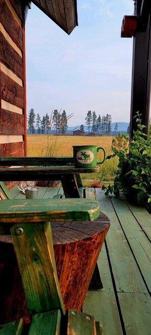 Une terrasse en bois avec un banc rustique et une table, donnant sur un champ et des arbres.