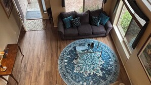 A spacious living area with a large round rug, a sofa with cushions, and a coffee table. There are two armchairs, a lamp, and a bookshelf. The room has large windows and a view of the outdoors. - Furnished, 31 day min. gated cul de sac
Las Sendas amenities incl., 3 car garage (Mesa)