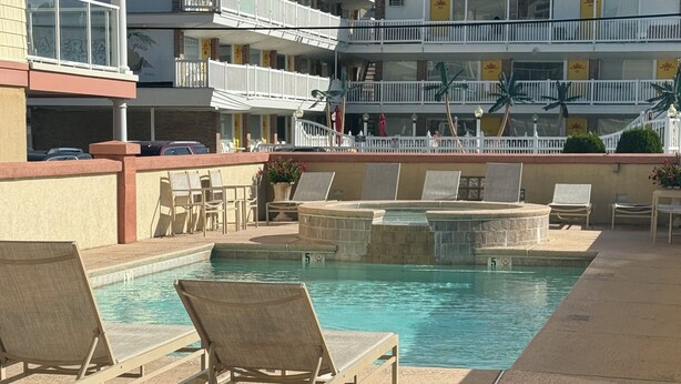 A pool area with lounge chairs and a building with balconies in the background. - SPACIOUS HOUSE WITH POOL OCEANVIEW 3 DECKS 4 MASTER CLOSE TO OCEAN AND BOARDWALK (Wildwood Crest)