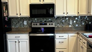 Una cucina con mobili bianchi, un forno a microonde nero, elettrodomestici in acciaio inossidabile e un pannello decorativo a parete.