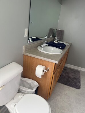 A bathroom with a wooden vanity, two sinks, a toilet, and a mirror.