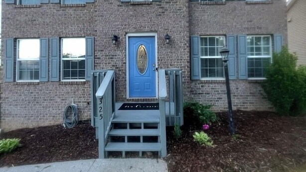 Un edificio in mattoni di due piani con una porta blu, un piccolo portico e un giardino piantumato sul davanti.