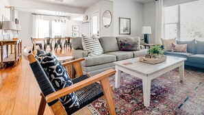 Ein geräumiges Wohnzimmer mit Sofa, Sesseln und Couchtisch, ein Essbereich mit Tisch und Stühlen sowie ein großes Fenster mit Vorhängen.