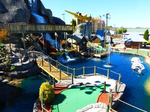 A water park with a wooden bridge, a large yellow airplane, and a water slide. - Premier Cabin in Eagle Springs Resort – King/Queen Beds, Hot tub, Community Pool (Sevierville)