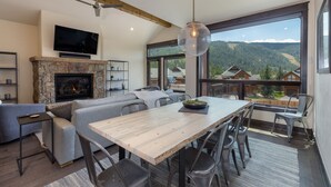 Una sala de estar moderna con chimenea de piedra, una amplia mesa de comedor y vistas a un paisaje montañoso a través de grandes ventanales.