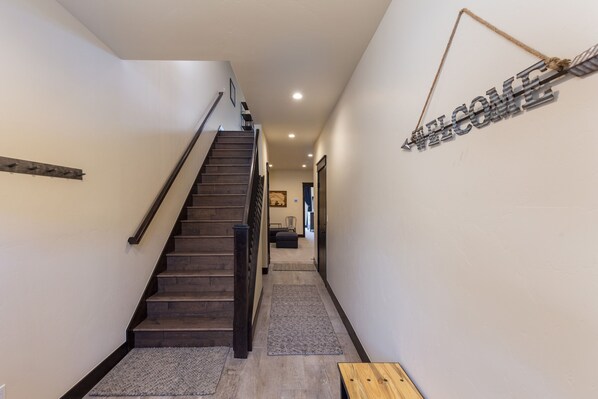 A modern interior with a wooden staircase, a welcome sign, and a hallway leading to a living area.