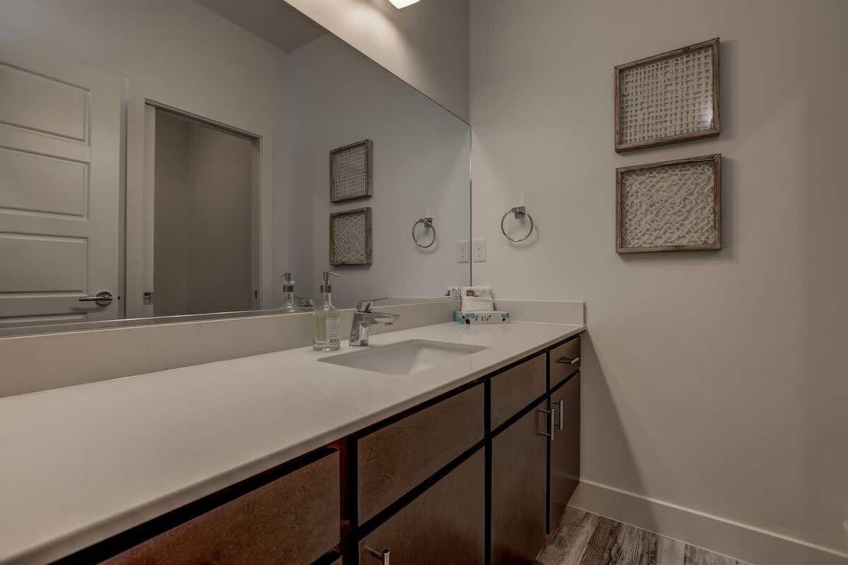 A modern bathroom with a large mirror, a white sink, and two towel rings on the wall.