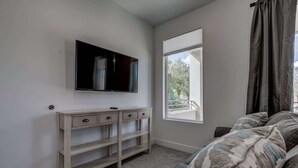 A bedroom with a bed, a TV mounted on the wall, a window, and a bedside table. - The Lofts #14 | Townhome Pool Resort | Poolside (Saint George)