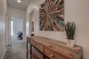 A hallway with a wooden console table, a potted plant, and a wall art piece.