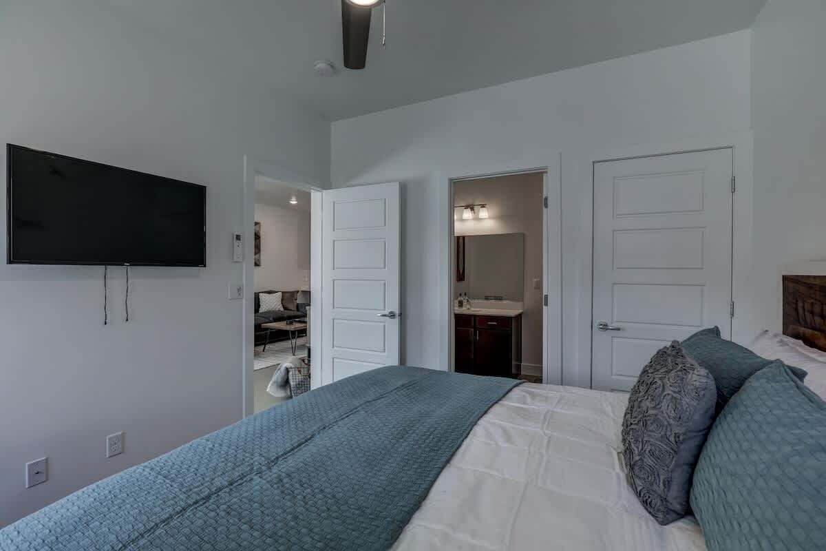A bedroom with a bed, a television mounted on the wall, and two doors leading to other rooms.