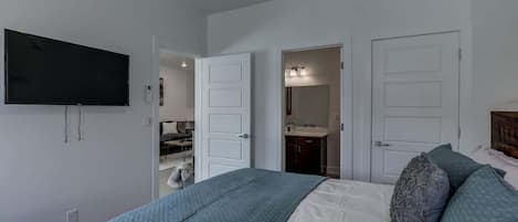 A bedroom with a bed, a television mounted on the wall, and two doors leading to other rooms.