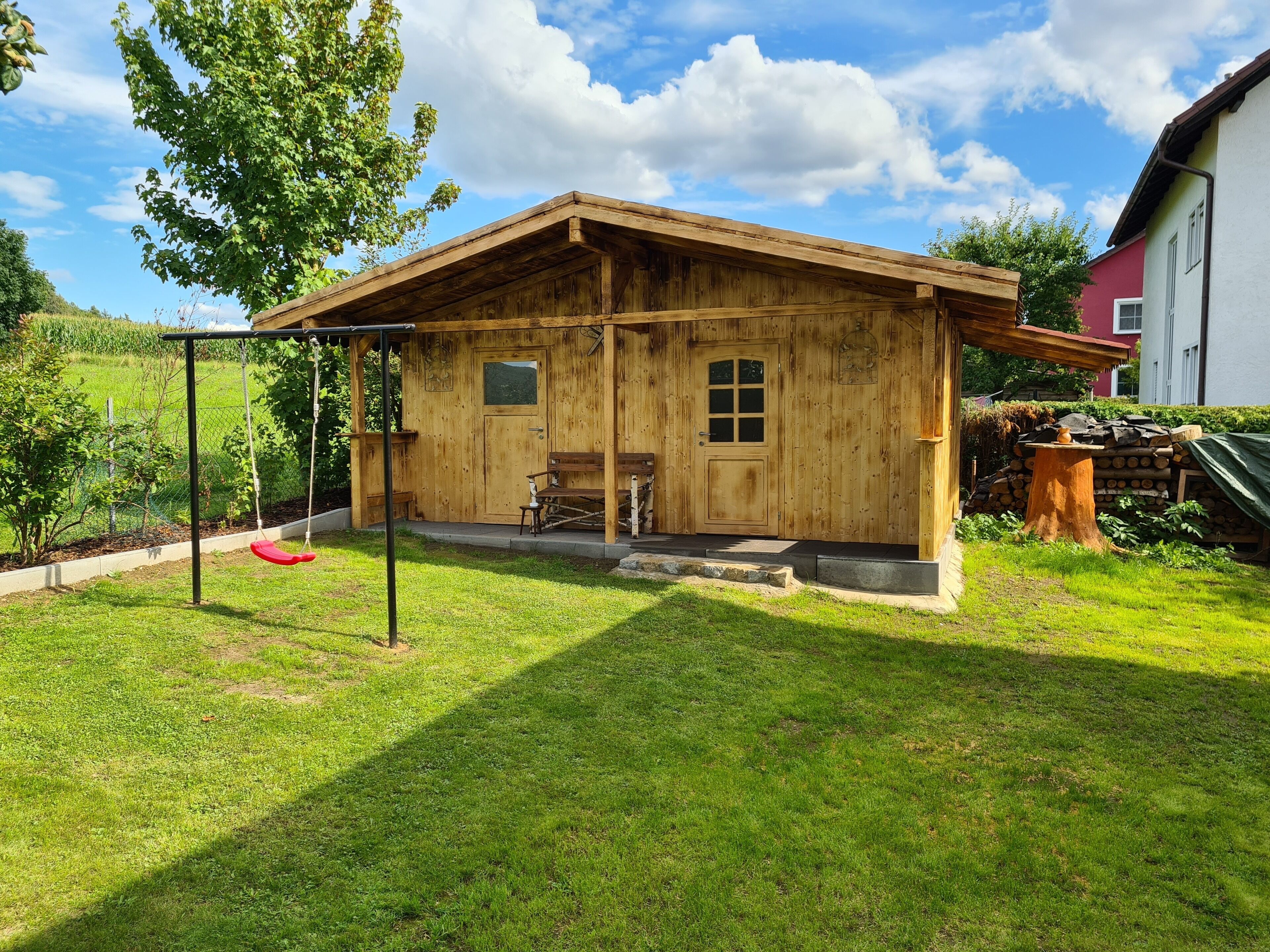 Une cabane en bois avec une véranda, une balançoire et une petite table sur laquelle est posé un vase.