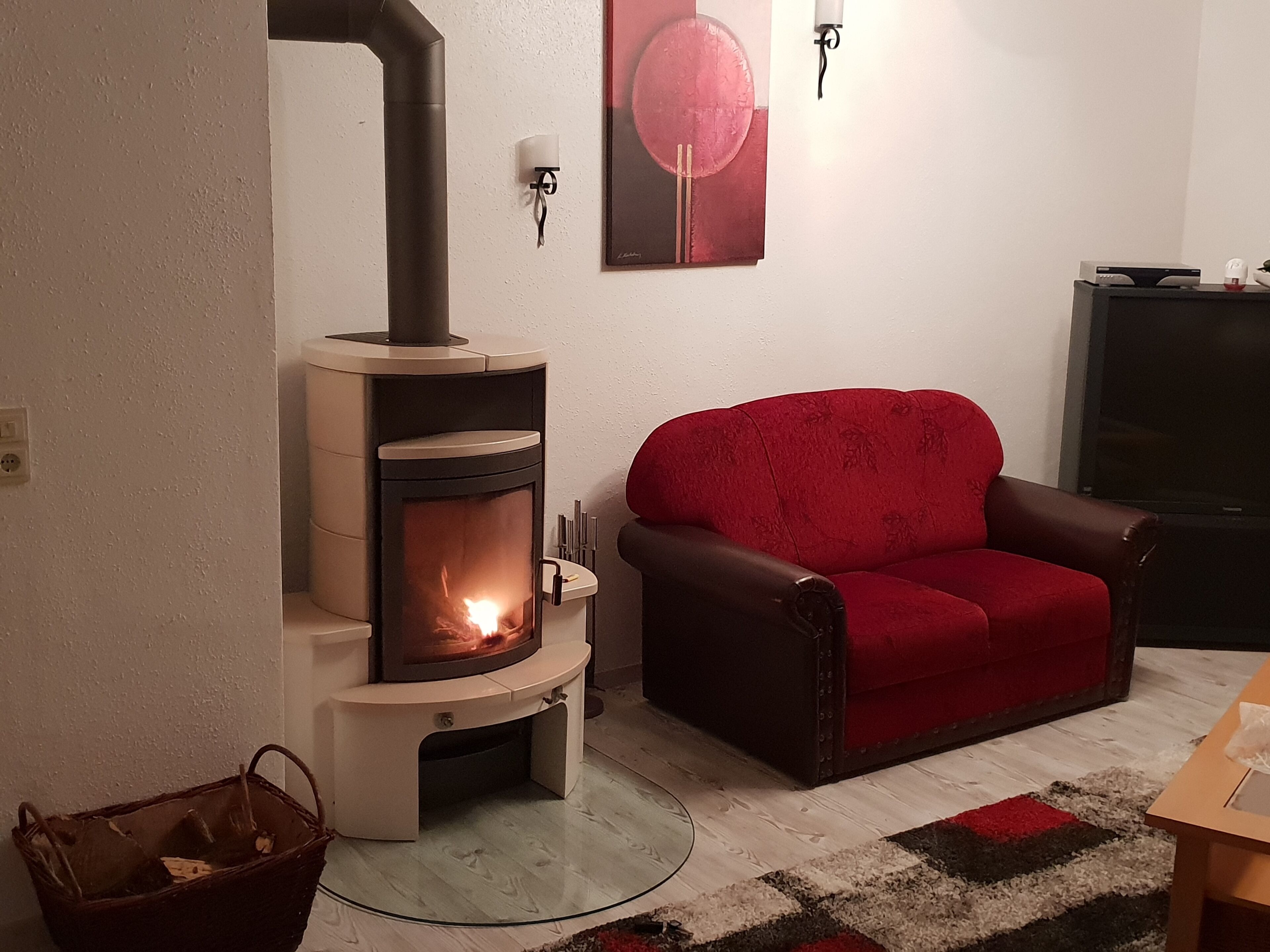 Een gezellige woonkamer met een houtkachel, een rode leren bank en een televisie op een dressoir.