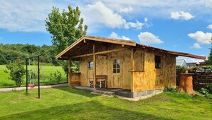 Une cabane en bois rustique, dotée d’une véranda, d’une balançoire et d’un mur en pierre.