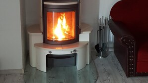 Un poêle à bois avec une façade en verre, une cheminée et un fauteuil rouge à proximité.