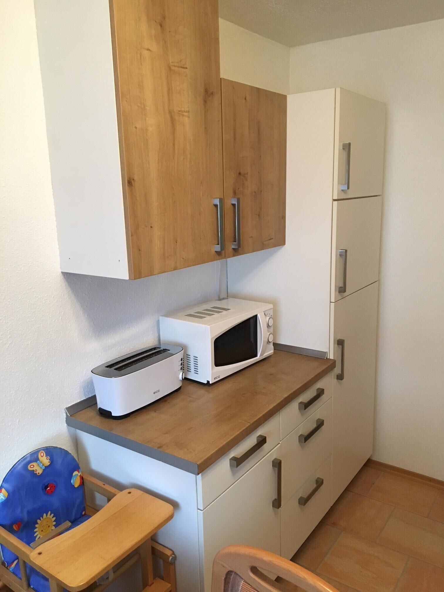 A compact kitchenette with a microwave, toaster, and wooden cabinets.