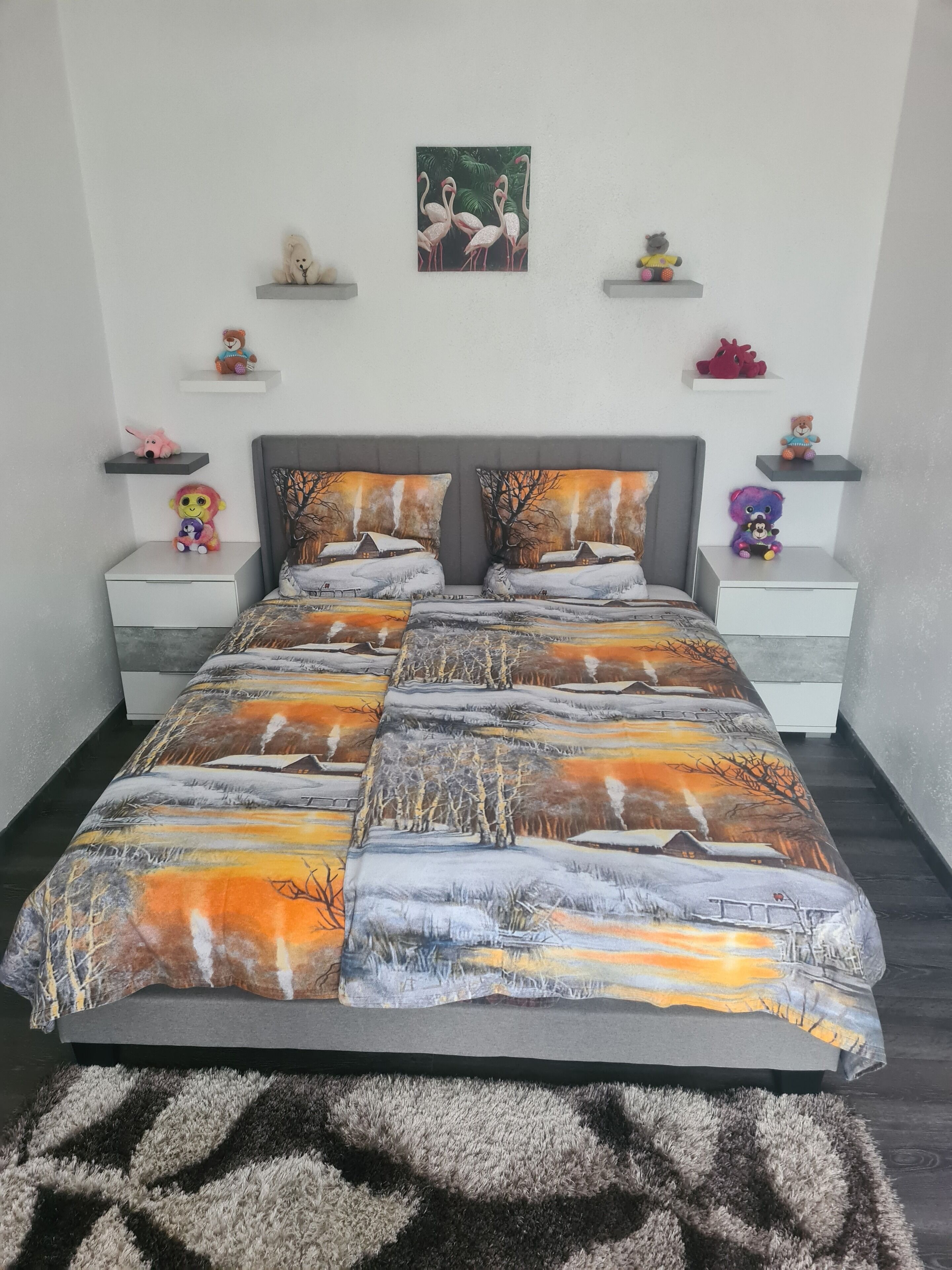 A bedroom with a large bed, two nightstands, a gray headboard, and a painting of flamingos on the wall.
