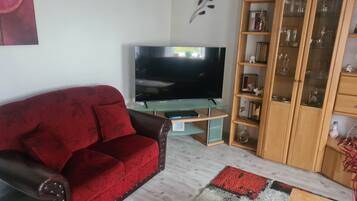 Ein Wohnzimmer mit einem roten Sofa, einem Flachbildfernseher, einer Holzkassette mit Glastüren und einem gemusterten Teppich.